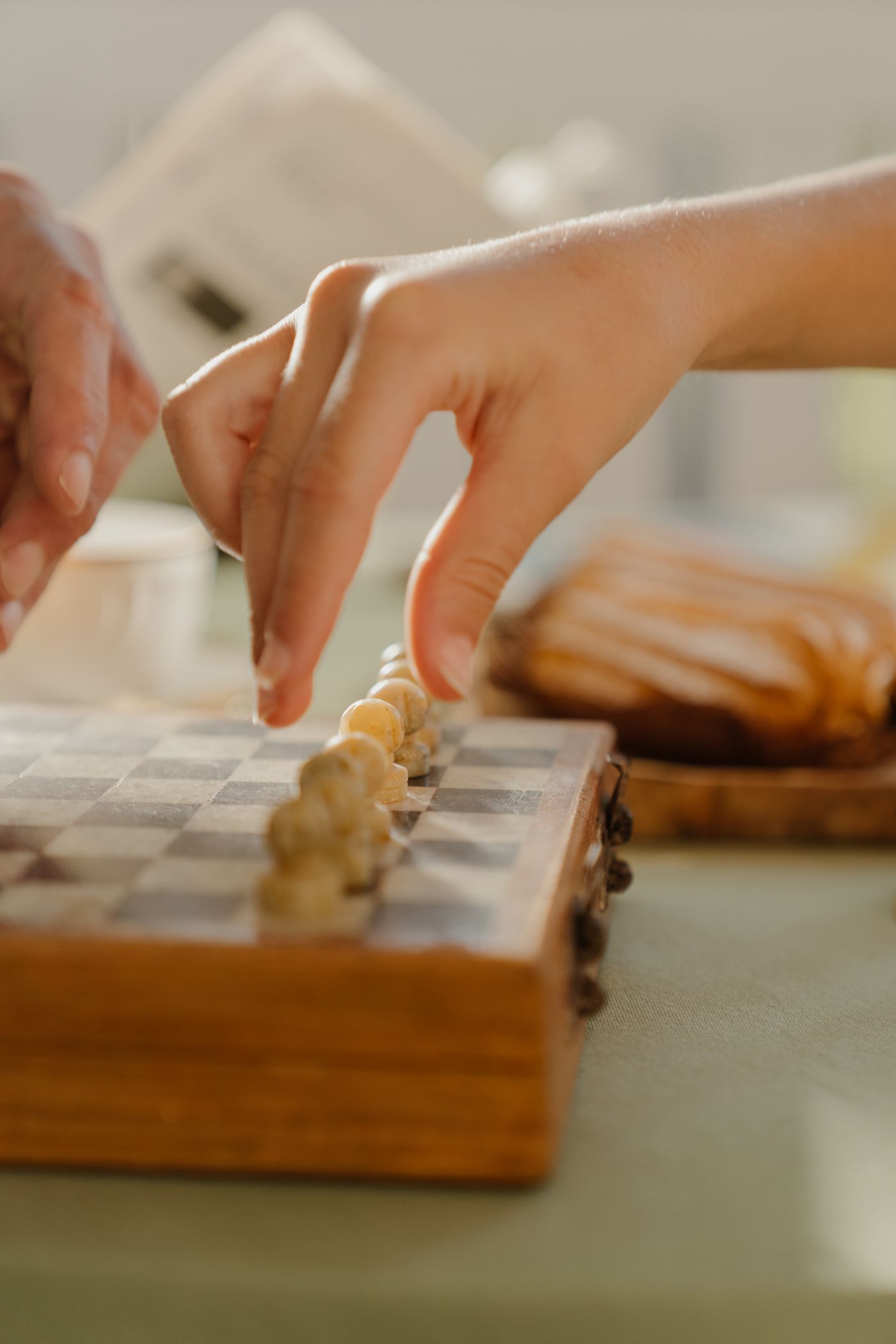 Two people playing a game of chess across a wooden board