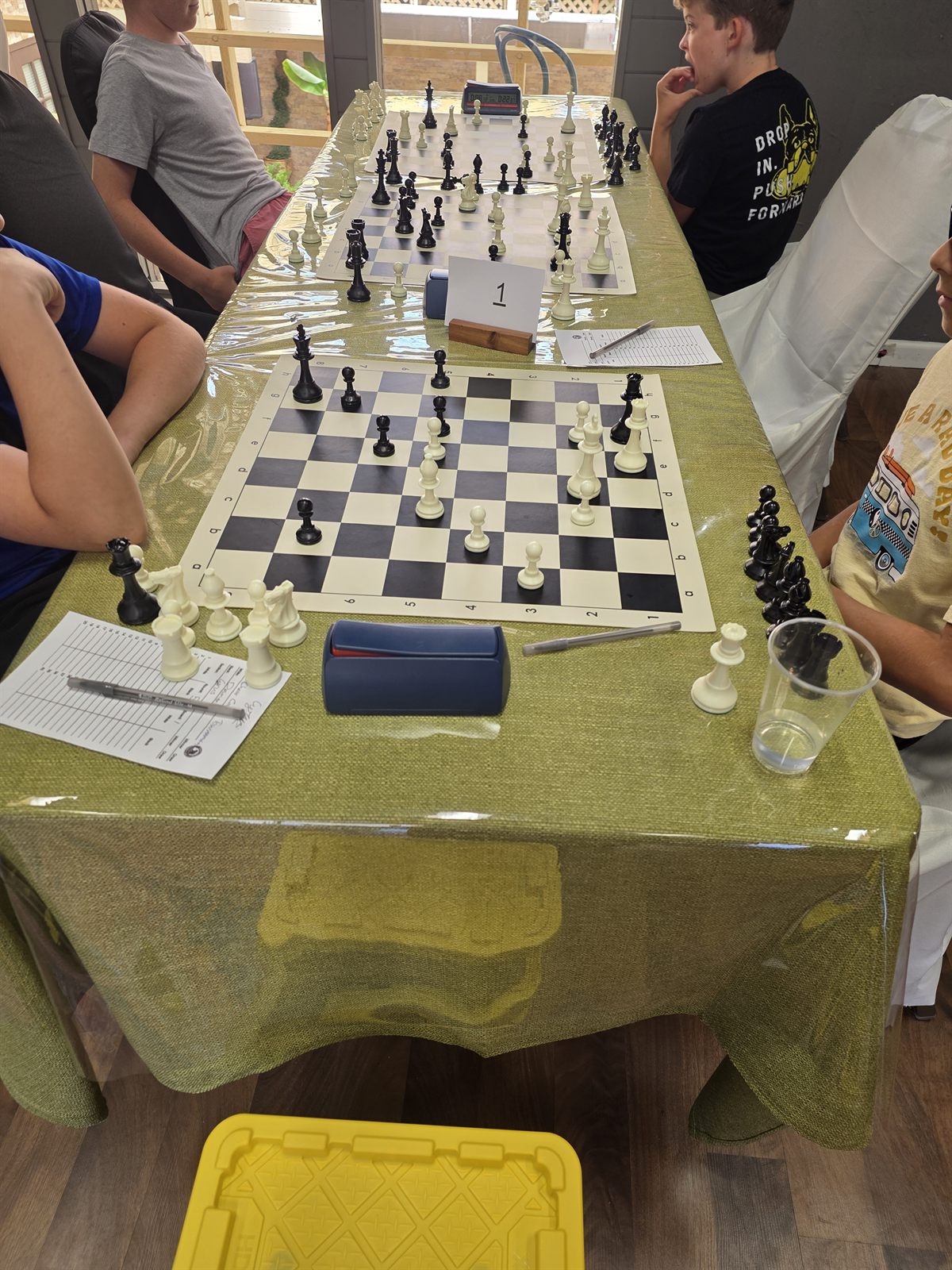 Two kids concentrating over a chess board with score sheets and a clock at Carmel Valley Chess Club