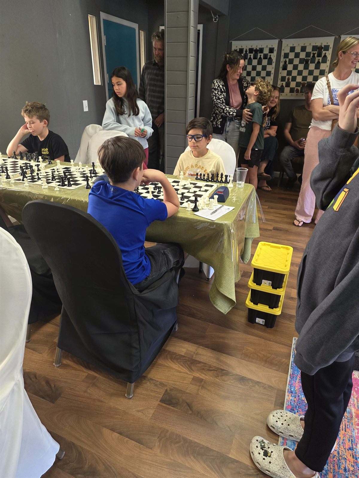 Kids playing chess while parents and family watch at a Carmel Valley Chess Club youth tournament